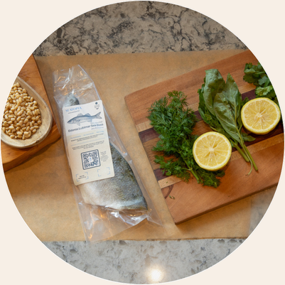 Packaged fish, lemon slices, herbs, and pine nuts on a kitchen counter.