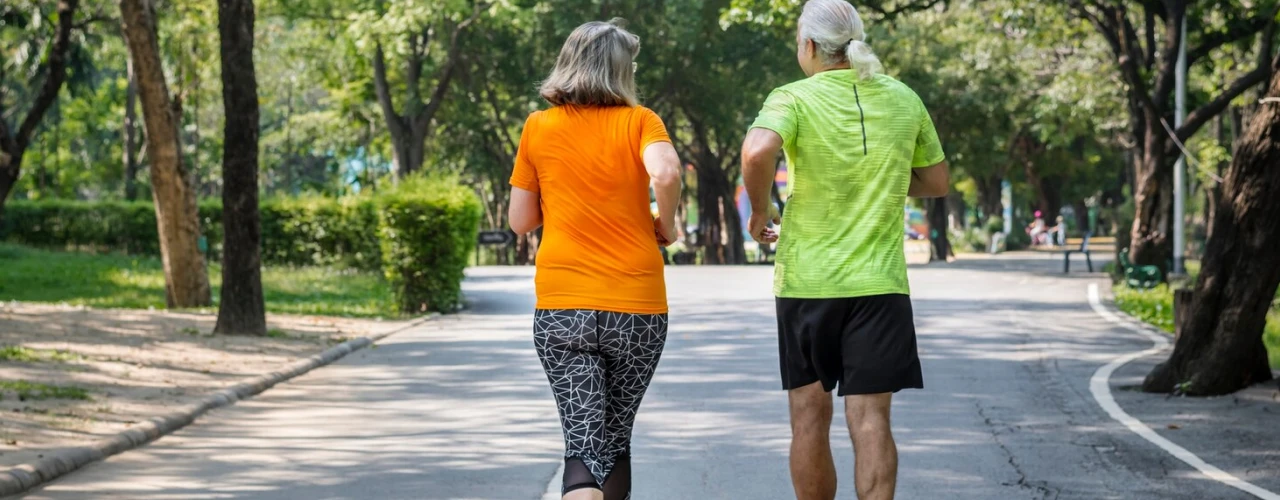 Two people jogging in a park with trees around them.