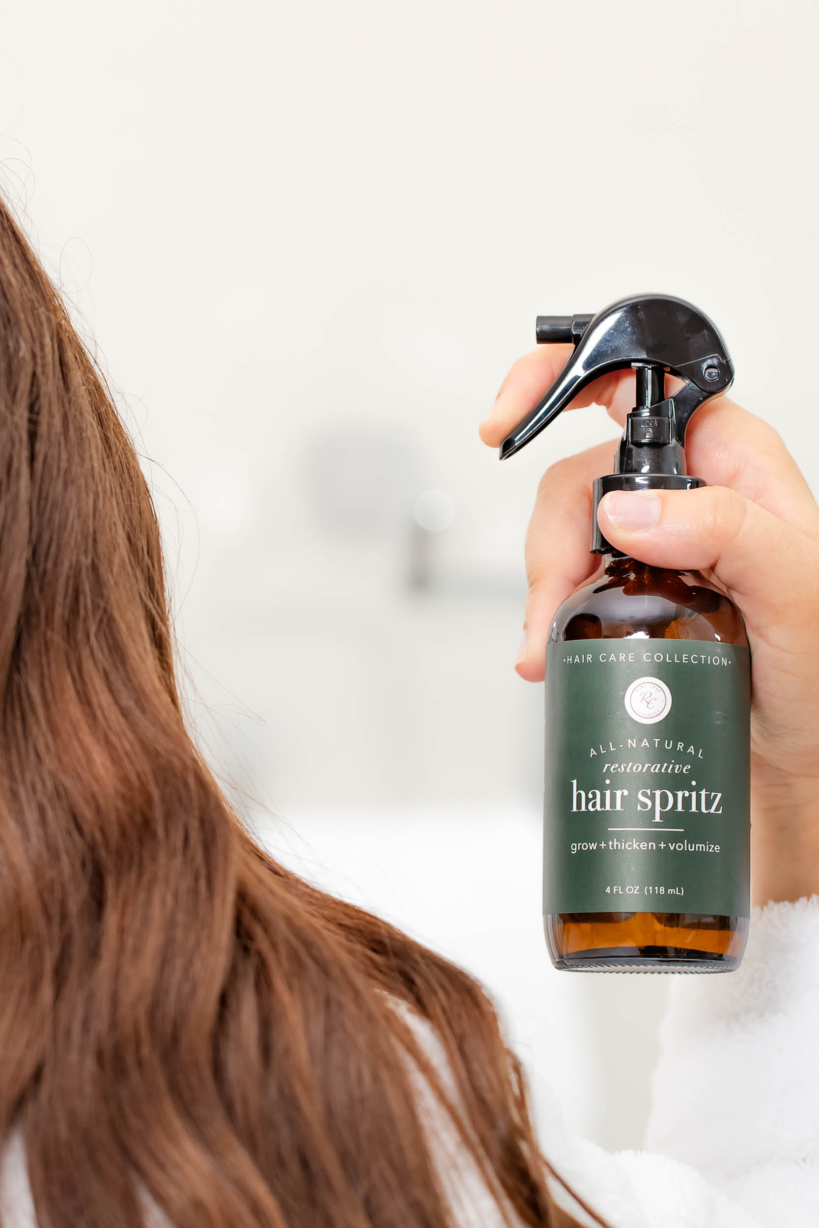 A person holds a bottle of hair spritz, preparing to spray it onto long, brown hair.