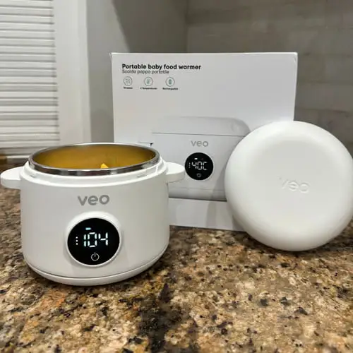 A white Veo portable baby food warmer with its lid and packaging on a countertop.