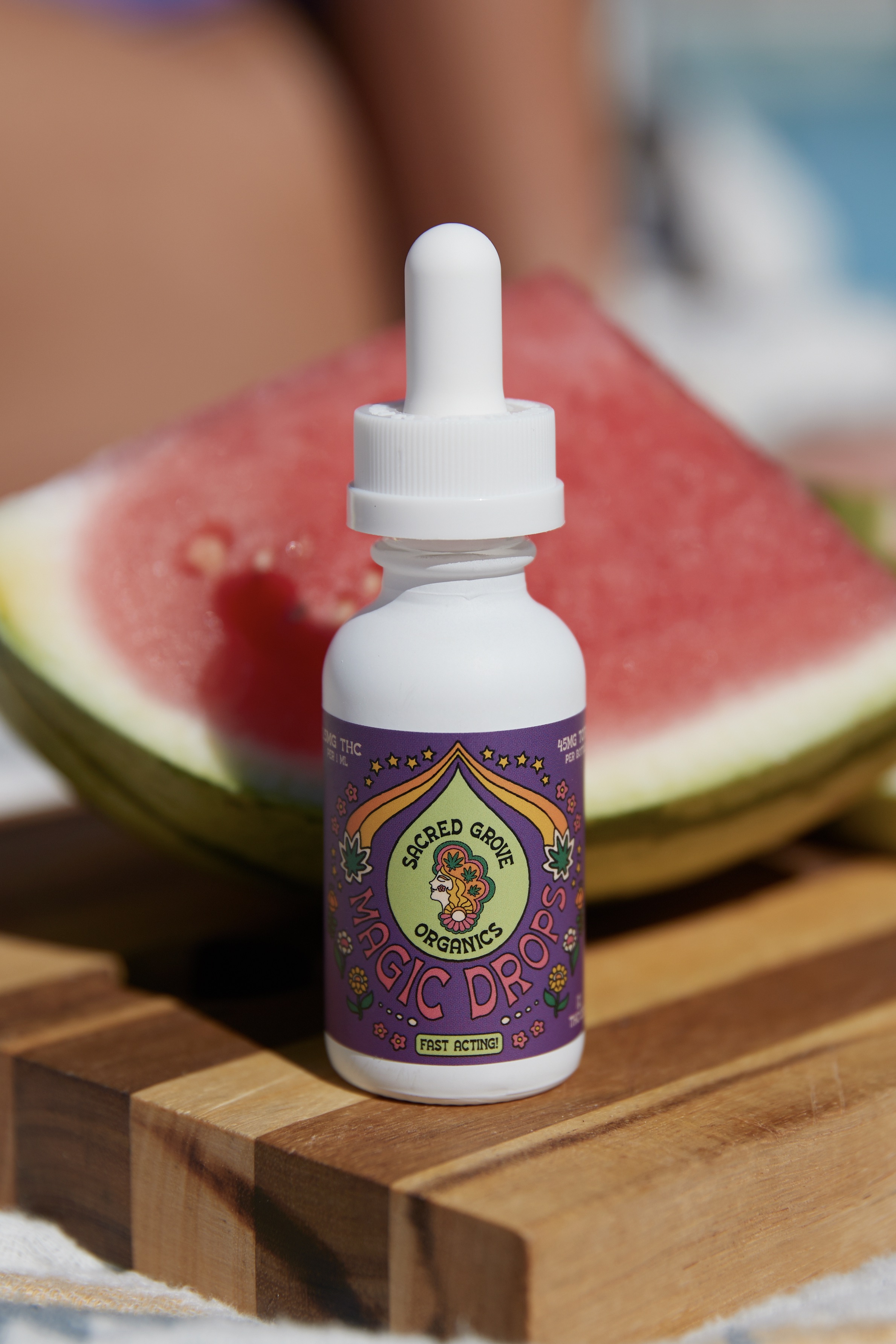 A bottle of Sacred Grove Organics Magic Drops in front of a watermelon slice.