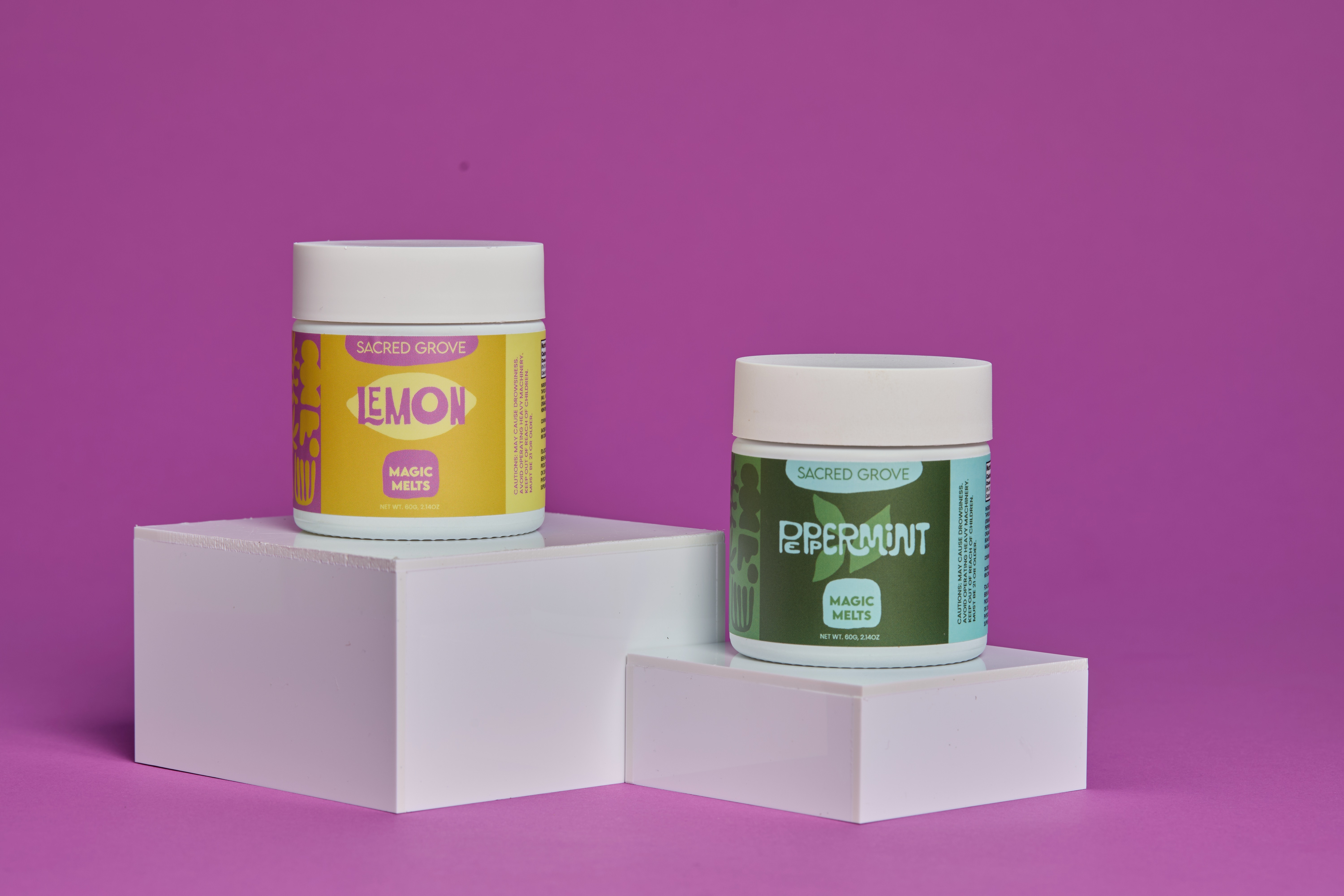 Two jars of Sacred Grove Magic Melts, lemon and peppermint, on white blocks against a purple background.