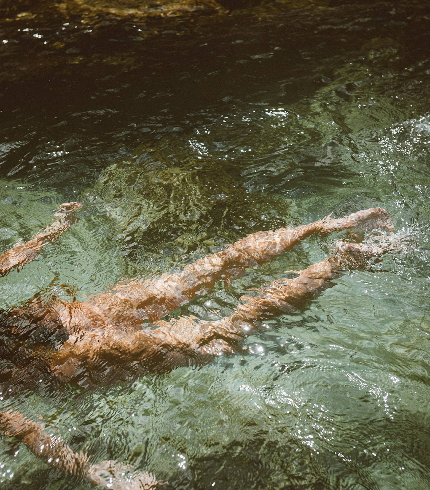 Person swimming underwater with legs visible through clear water.