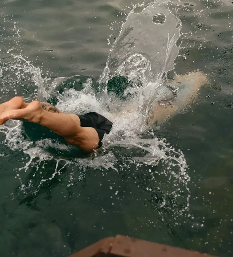 A person wearing black swim trunks dives headfirst into dark water, creating a large splash.