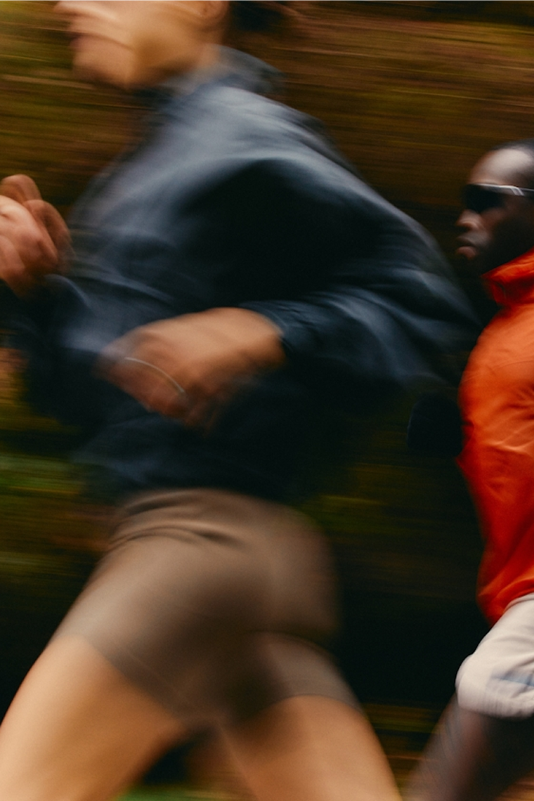 A motion-blurred, close-up action shot of two people running side-by-side outdoors.