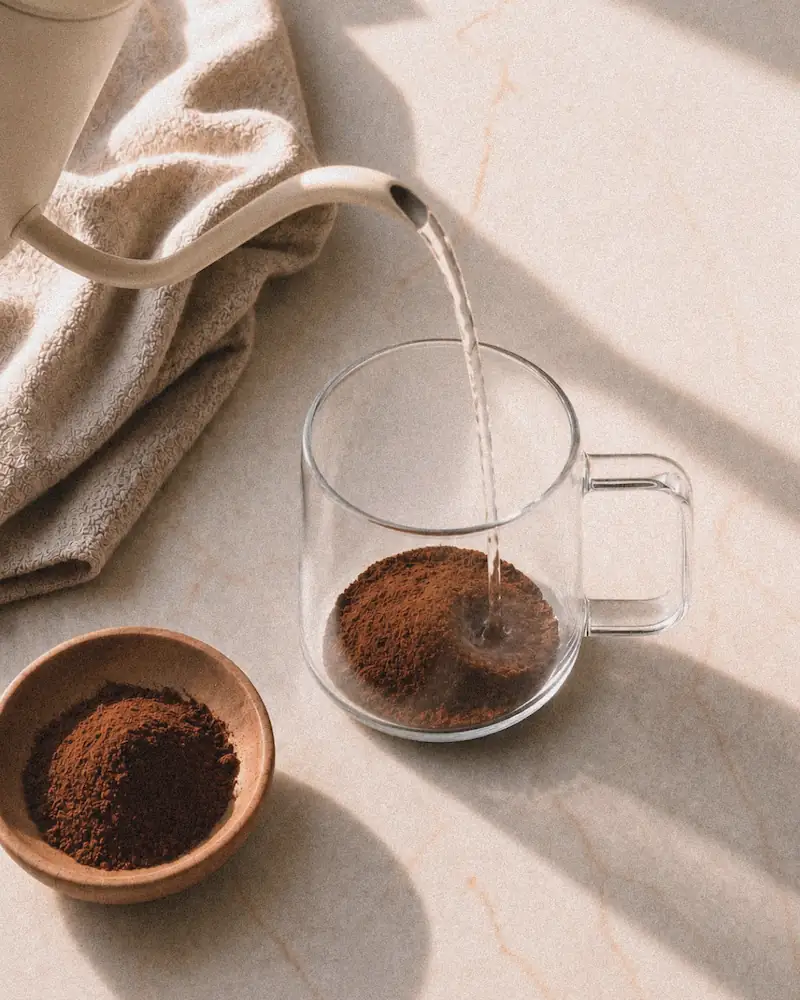 A thick, frothy chocolate drink being stirred with a wooden spoon in a clear glass mug.