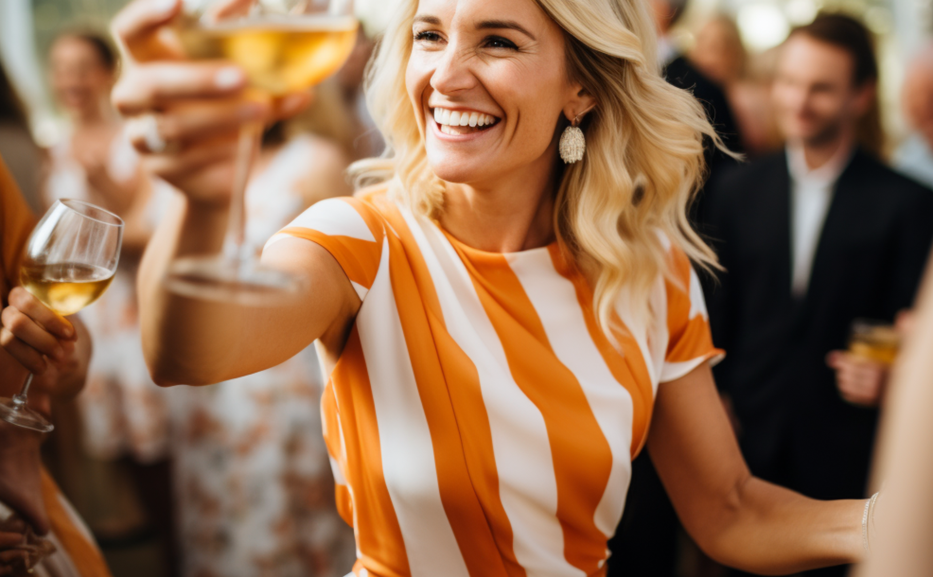 A smiling blonde woman in an orange and white striped dress raises a glass of wine.