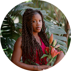 Person holding flowers, standing in front of tropical plants.