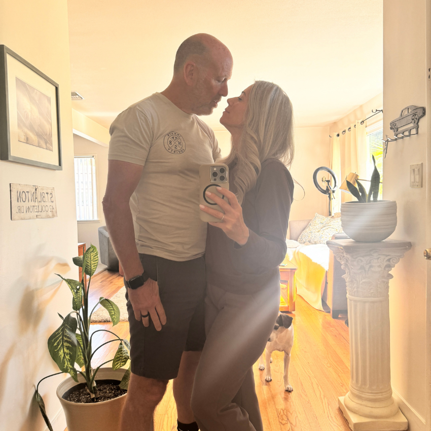 Couple taking a mirror selfie with a dog in a bright living room.