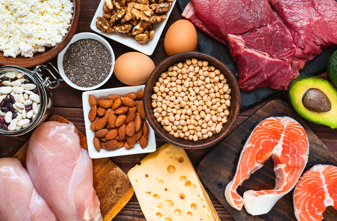 Assorted foods including meat, fish, nuts, cheese, and eggs on a wooden table.