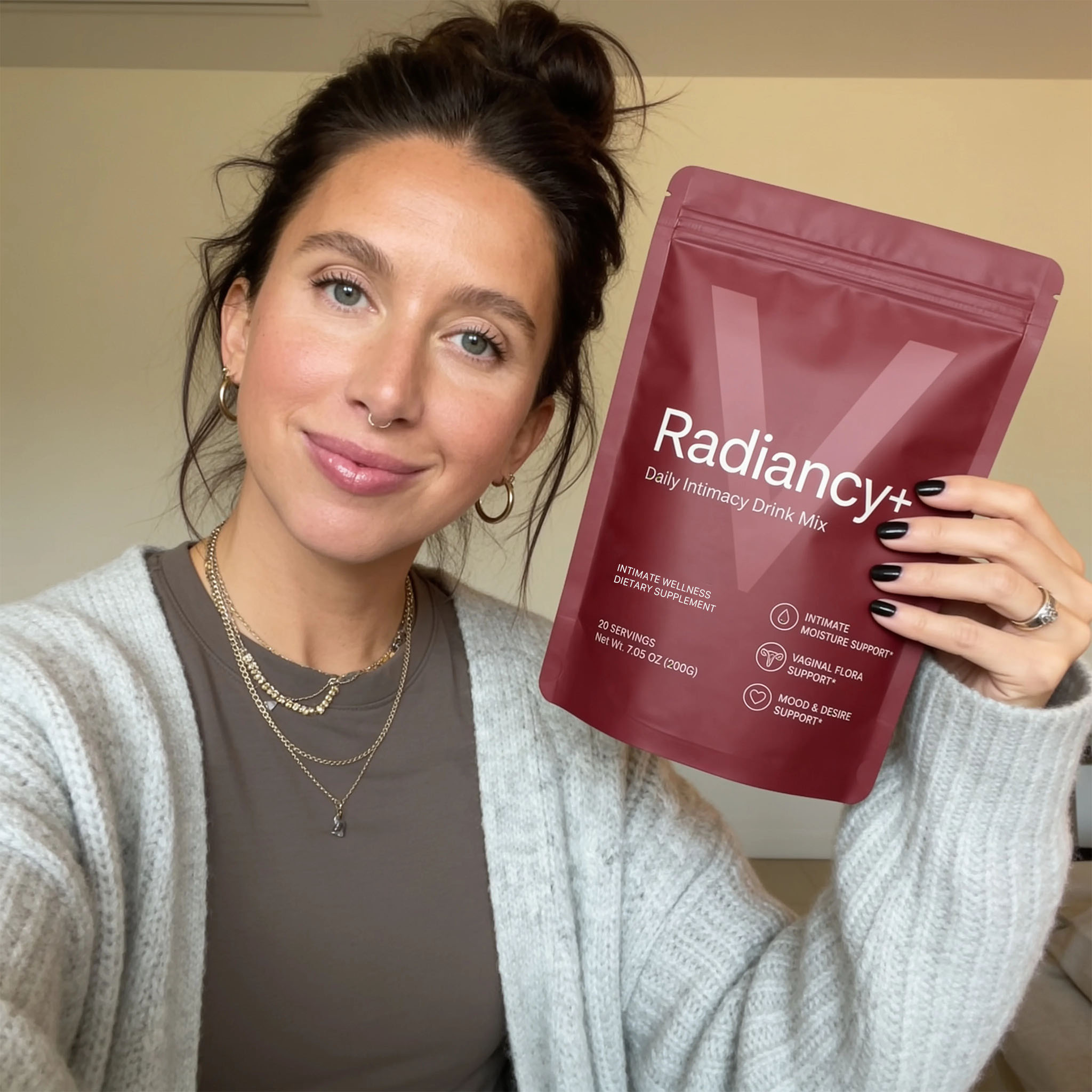 A smiling woman with her hair in a bun holds up a red pouch of Radiancy+ drink mix.