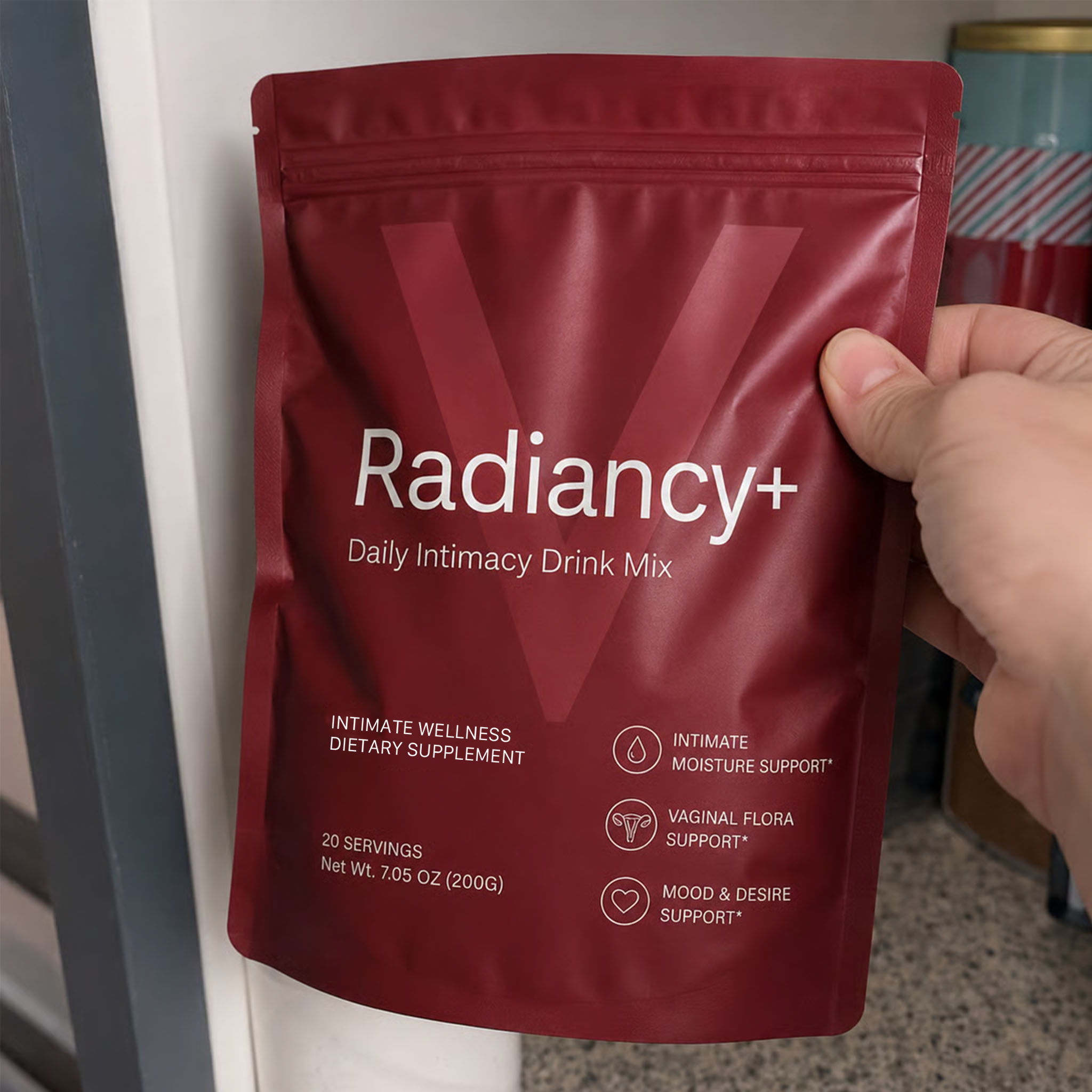 A hand holds a red pouch of Radiancy+ Daily Intimacy Drink Mix against a neutral background.