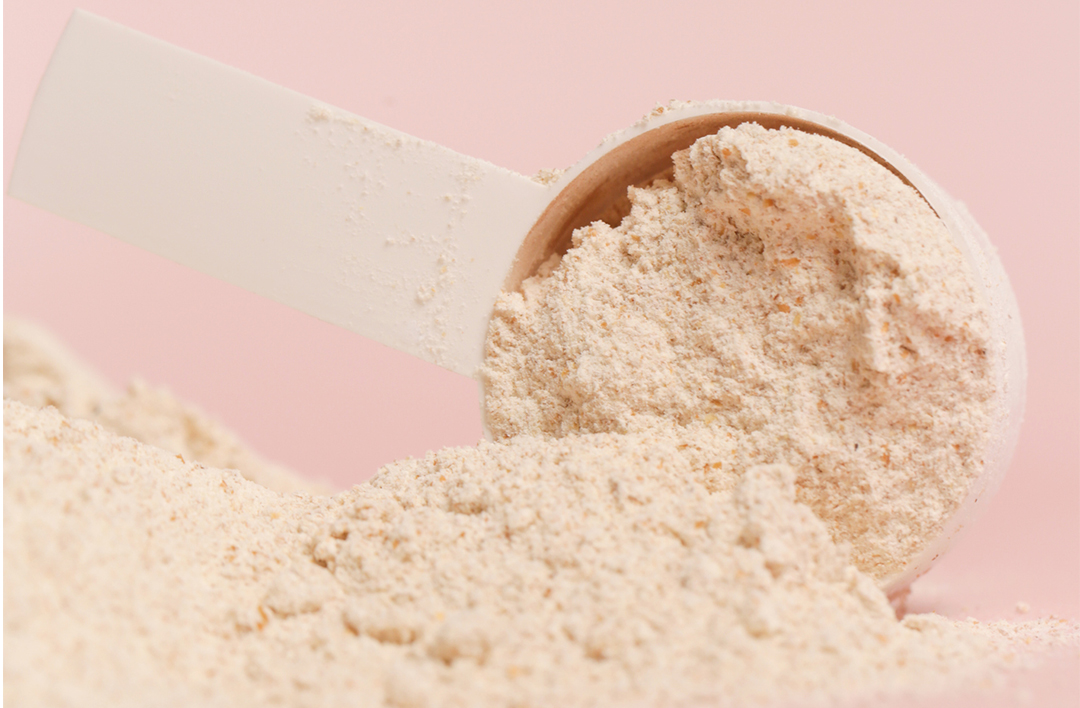 Scoop of powder against a pink background.