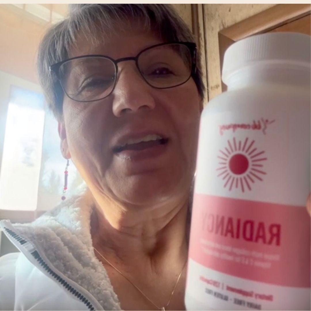 A woman with short hair and glasses holds up a white bottle with a pink label that reads 'RADIANCY'.