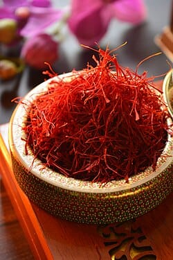 A close-up of a small, ornate bowl overflowing with bright red saffron threads.