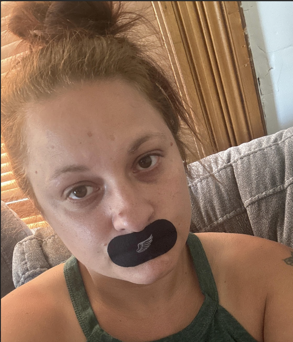 Person with a black patch over their mouth, sitting on a couch.