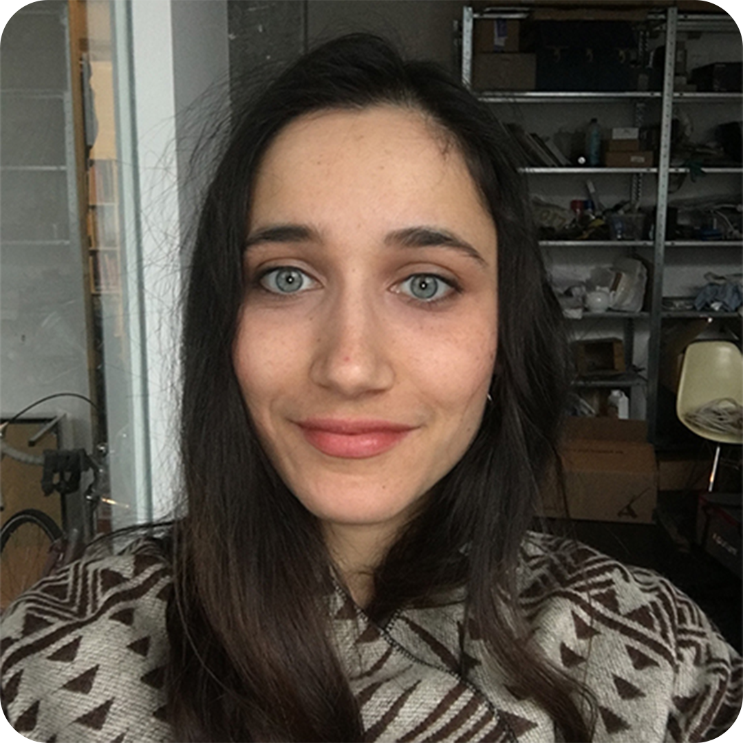 Person with long dark hair smiling in a room with shelves and boxes.