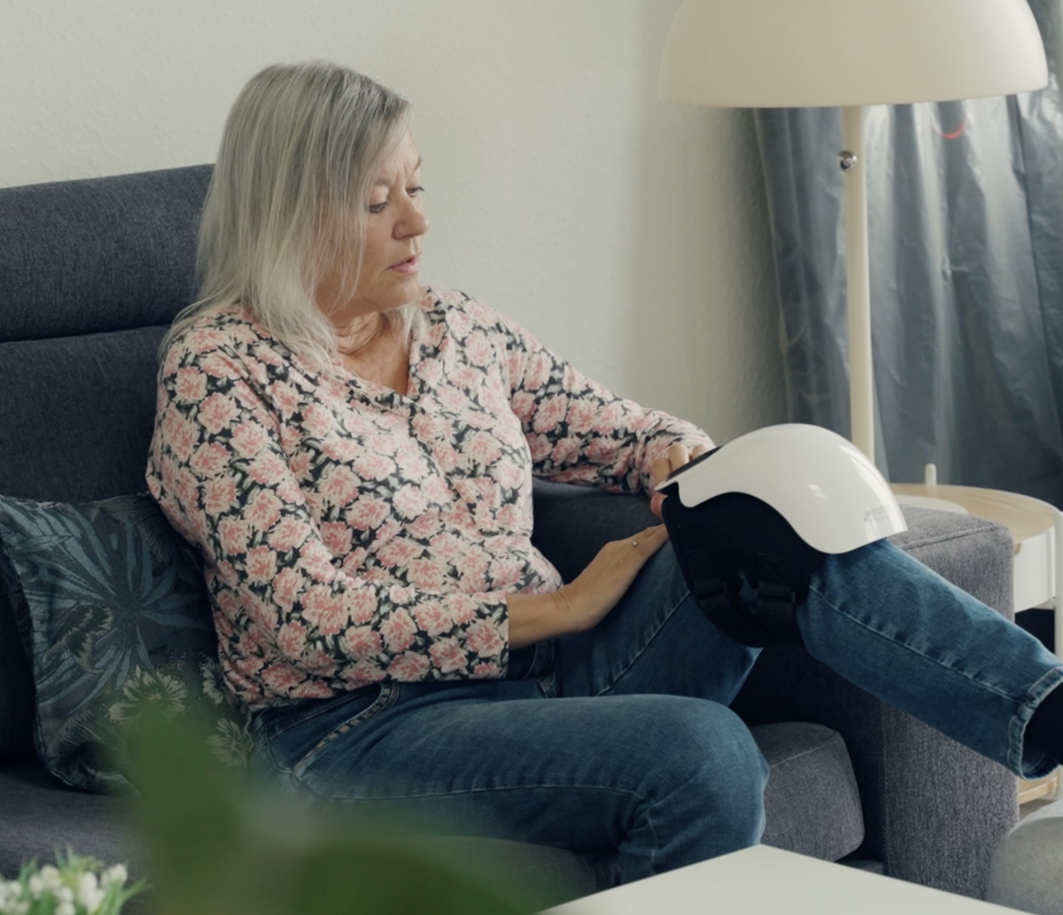 Person sitting on a couch holding a helmet-like device on their knee.