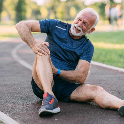 Elderly man sitting on track, holding his knee in pain.