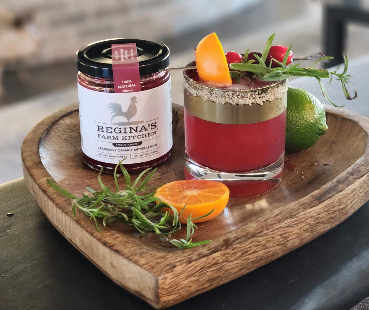 Wooden tray with cranberry-orange drink, fruit spread, herbs, orange, and lime.