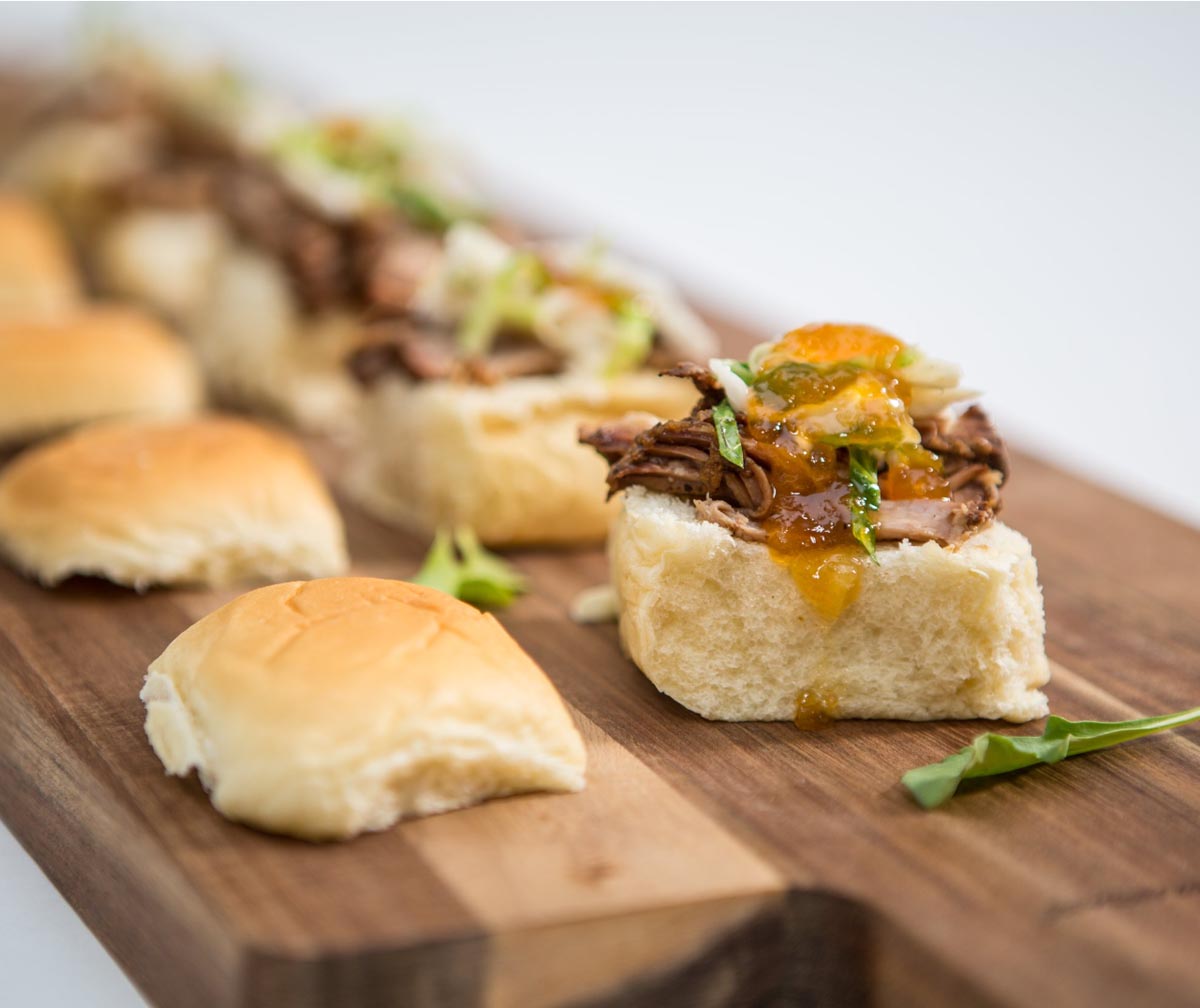 Mini beef sliders with garnish on a wooden board.