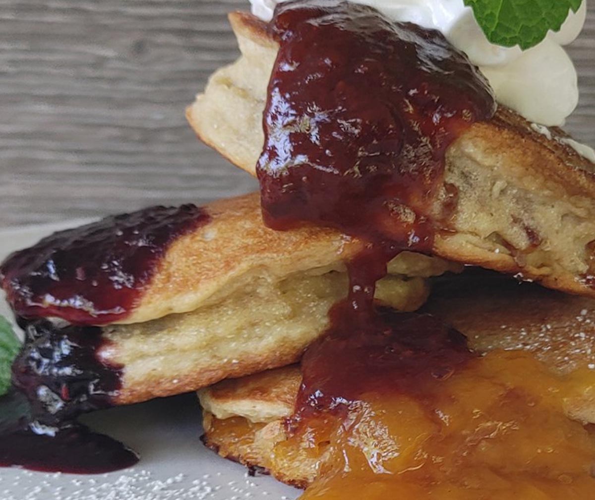 Stack of pancakes with berry and peach sauces, topped with cream and mint.