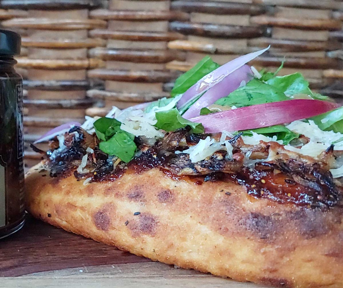 Gourmet pizza slice with toppings of greens, onions, and cheese on a wooden surface.