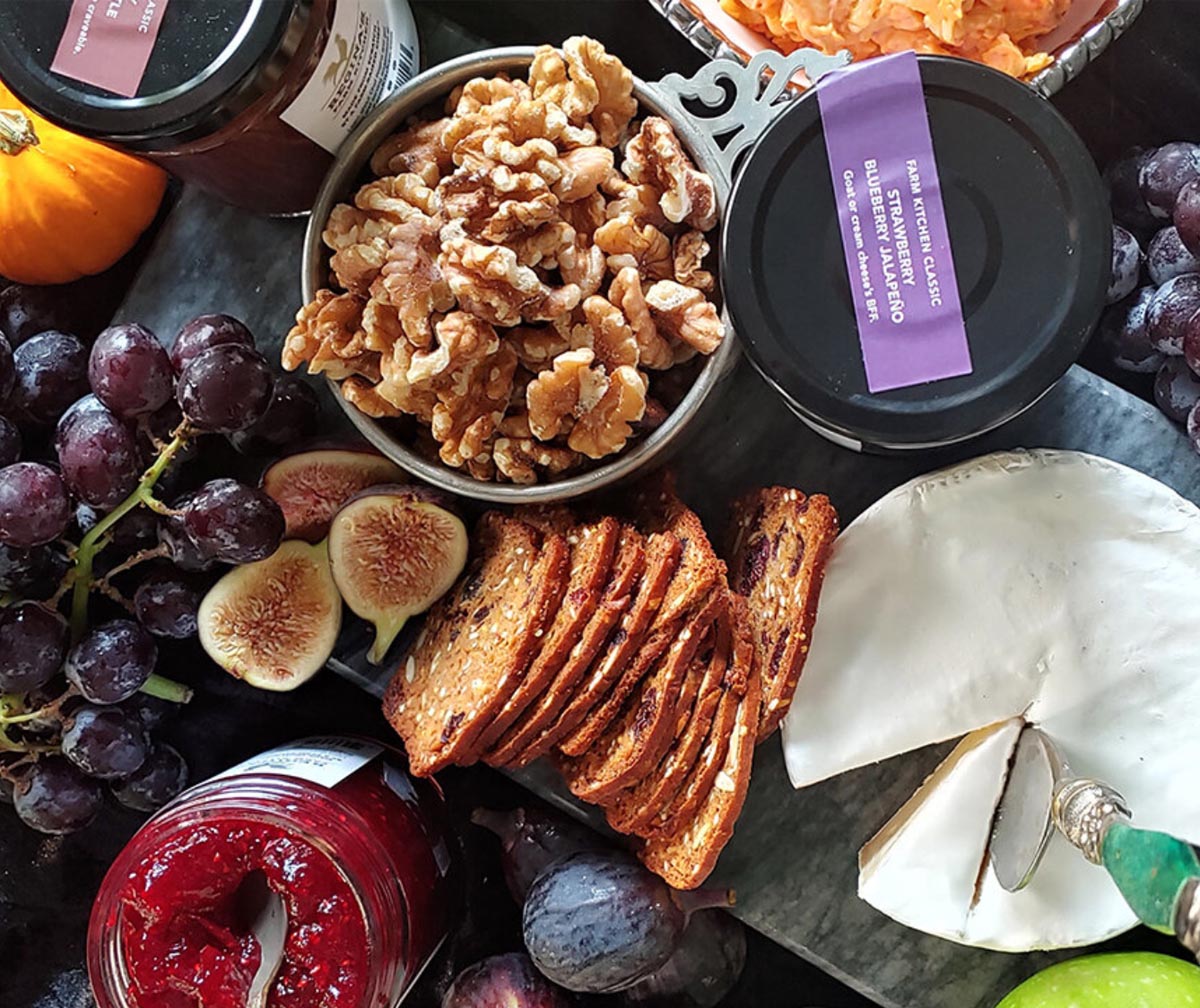 Cheese board with walnuts, grapes, figs, preserves, and sliced bread.