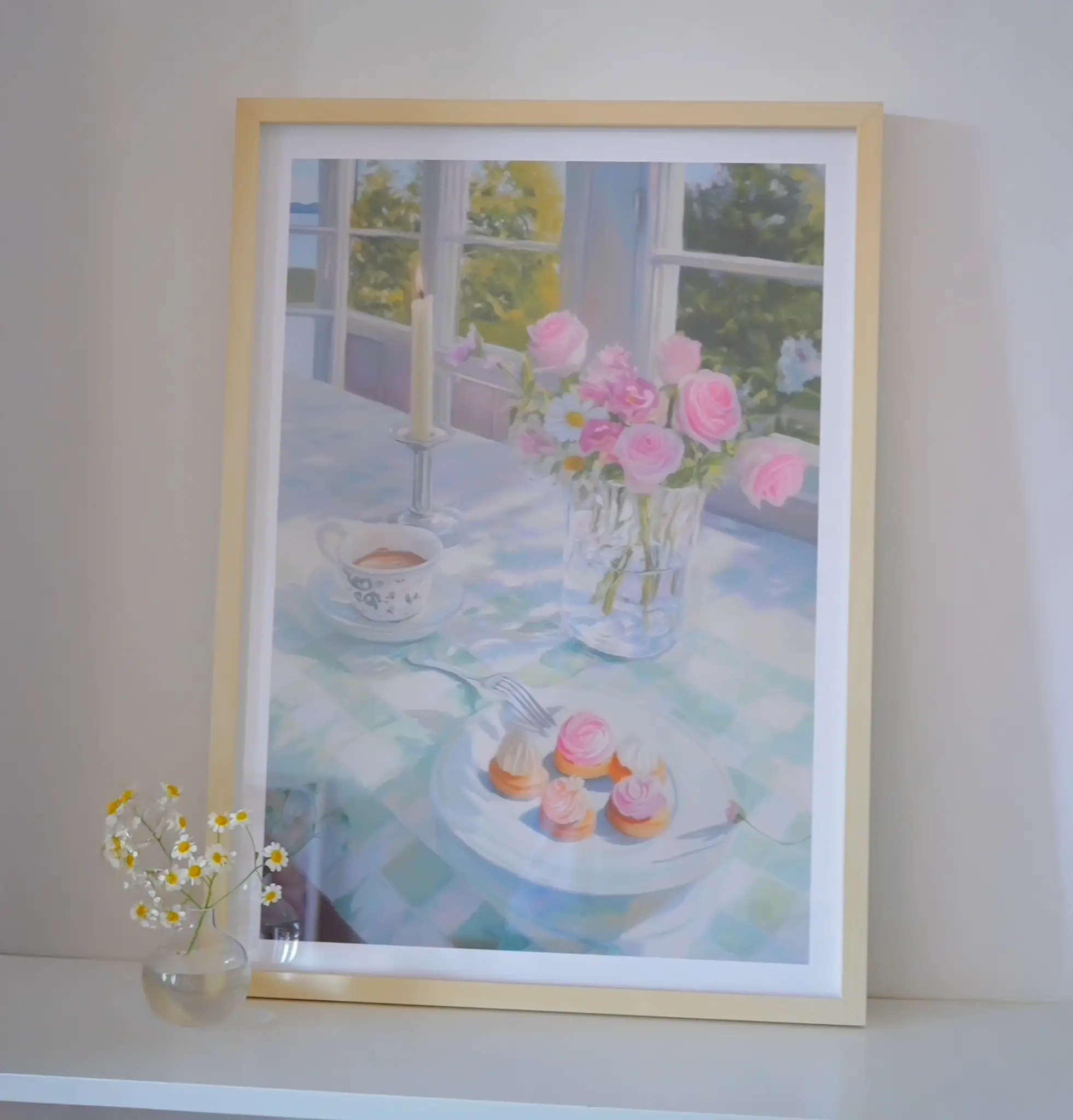 Framed painting of a table with flowers, candle, and pastries.