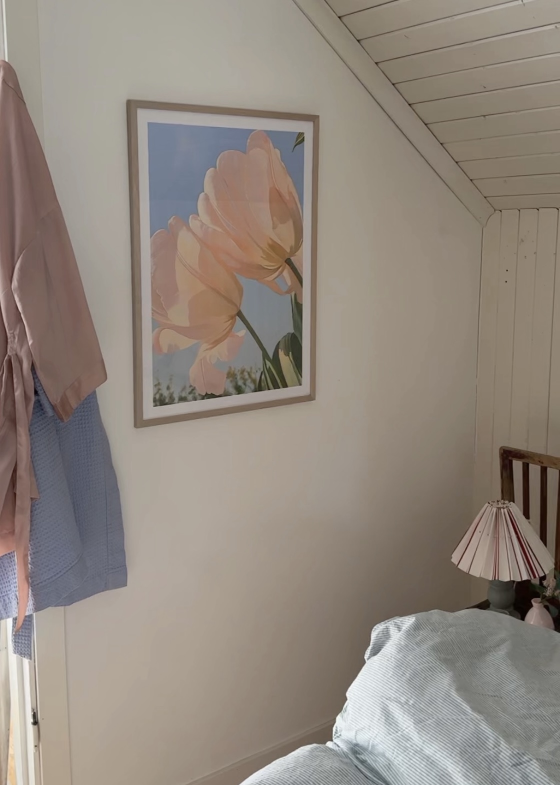 Bedroom with floral artwork, clothes hanging, and a lamp on a side table.