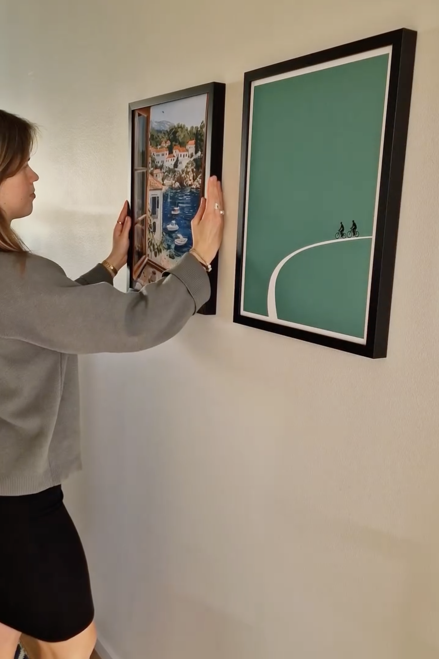 Person hanging framed artwork on a wall.