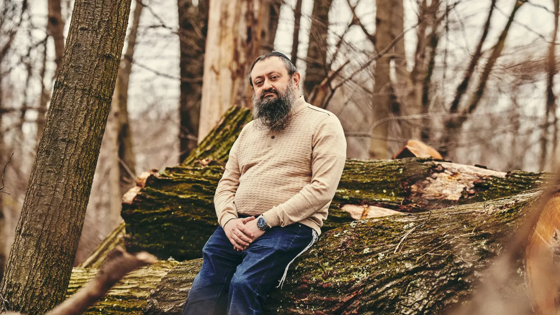 Man sitting on a fallen tree in a forest.