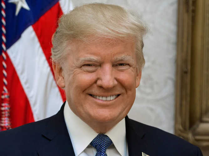 Smiling man in a suit with an American flag in the background.
