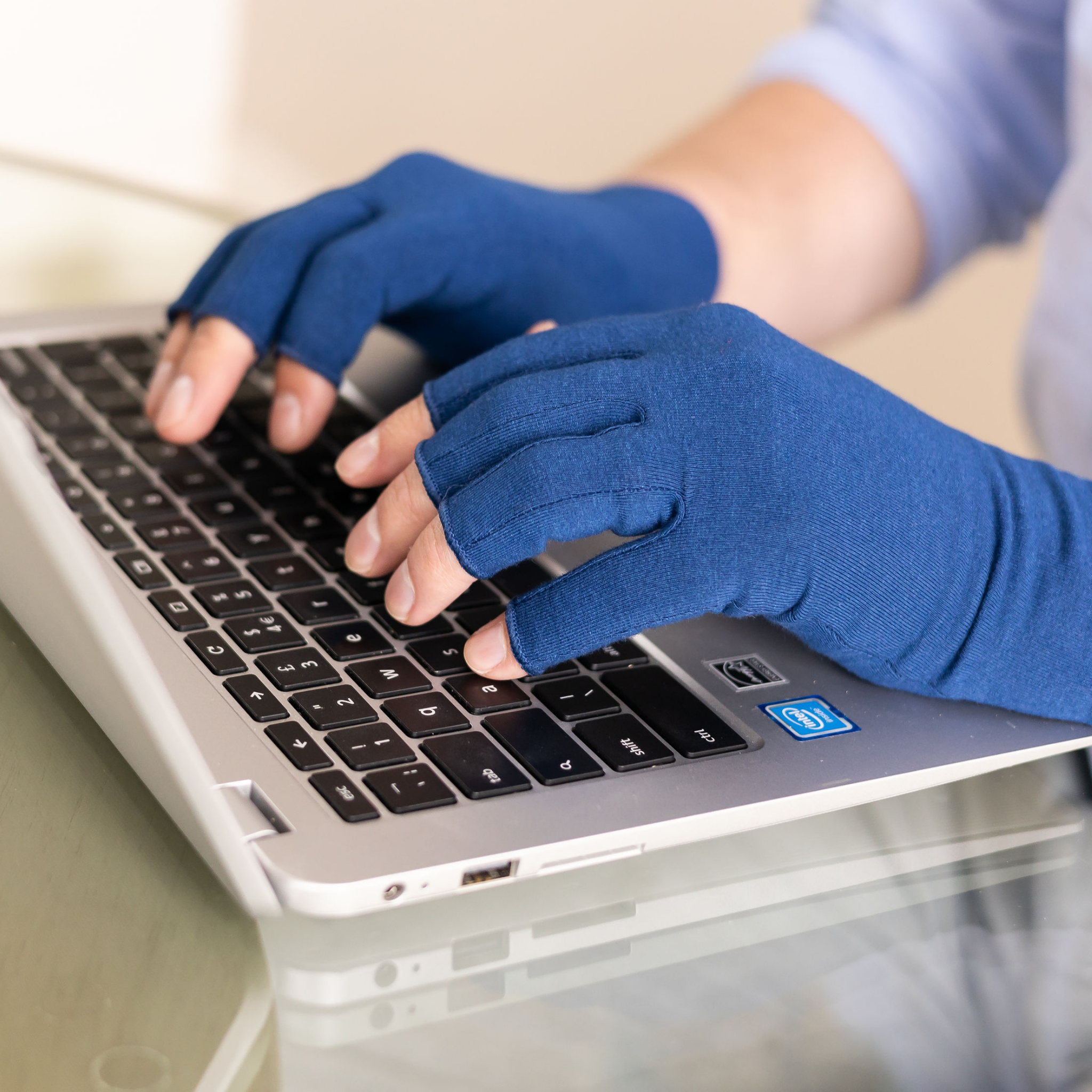 Person typing on a laptop wearing blue fingerless gloves.