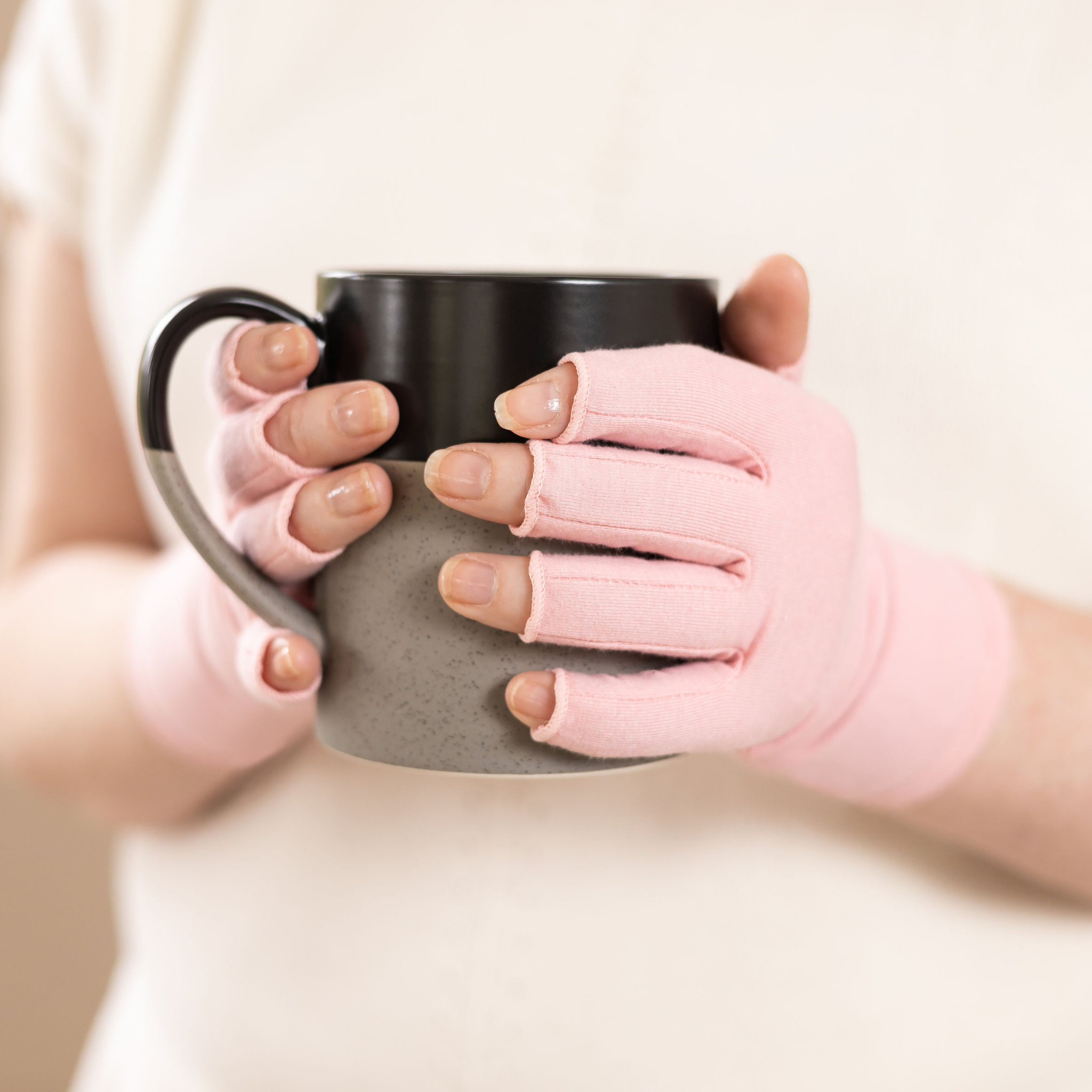 Person holding a mug wearing pink fingerless gloves.