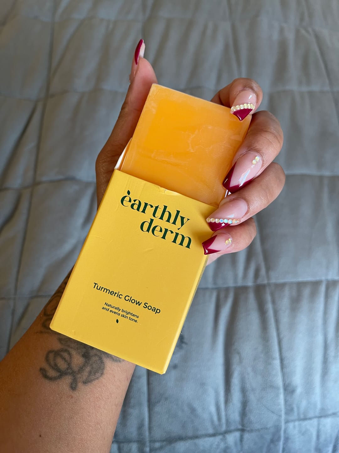 Hand holding a yellow box of turmeric glow soap with manicured nails.