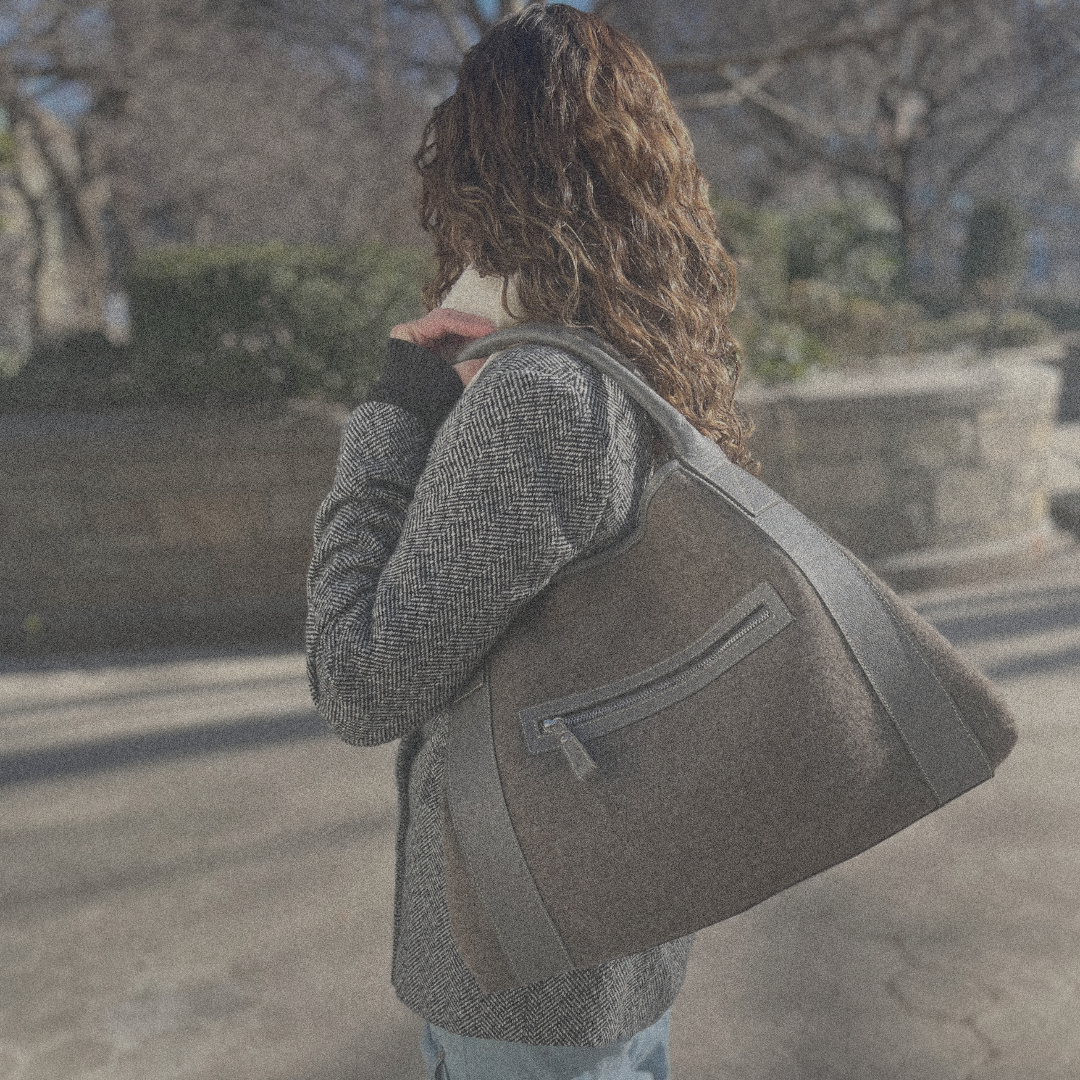 Person with curly hair carrying a large brown shoulder bag outdoors.