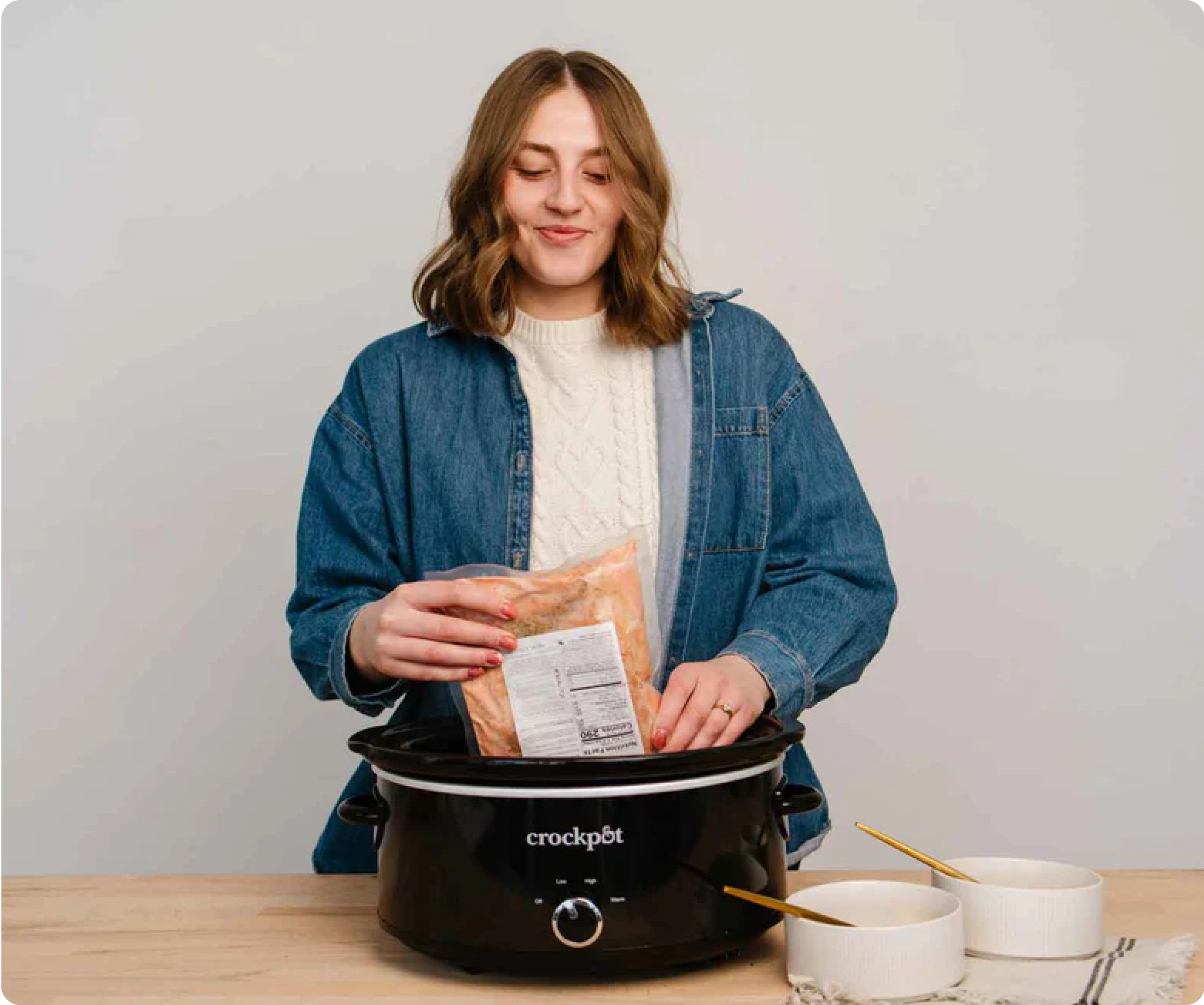 Person placing food package into a crockpot on a wooden table.