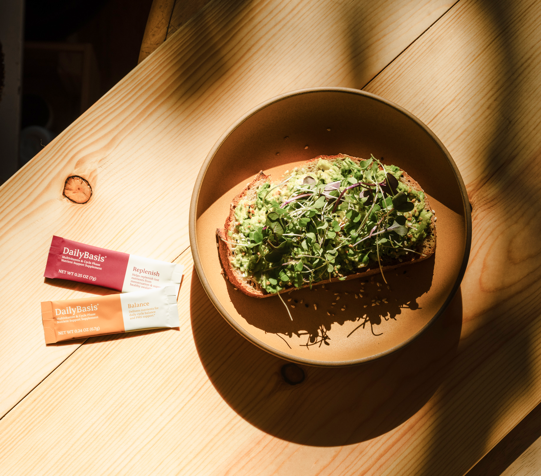 DailyBasis Cycle Routine Replenish and Balance supplement stick packs beside a healthy avocado toast meal on a wooden table