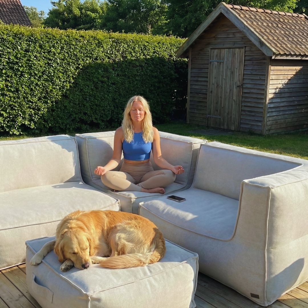 A woman meditates on an outdoor sofa while her golden retriever sleeps on an ottoman nearby.