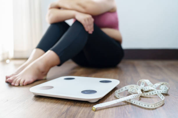 Person sitting near a scale and measuring tape on wooden floor.