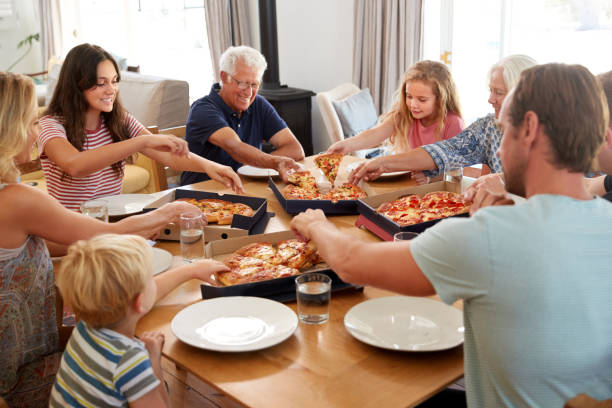 Family gathering around a table eating pizza together.