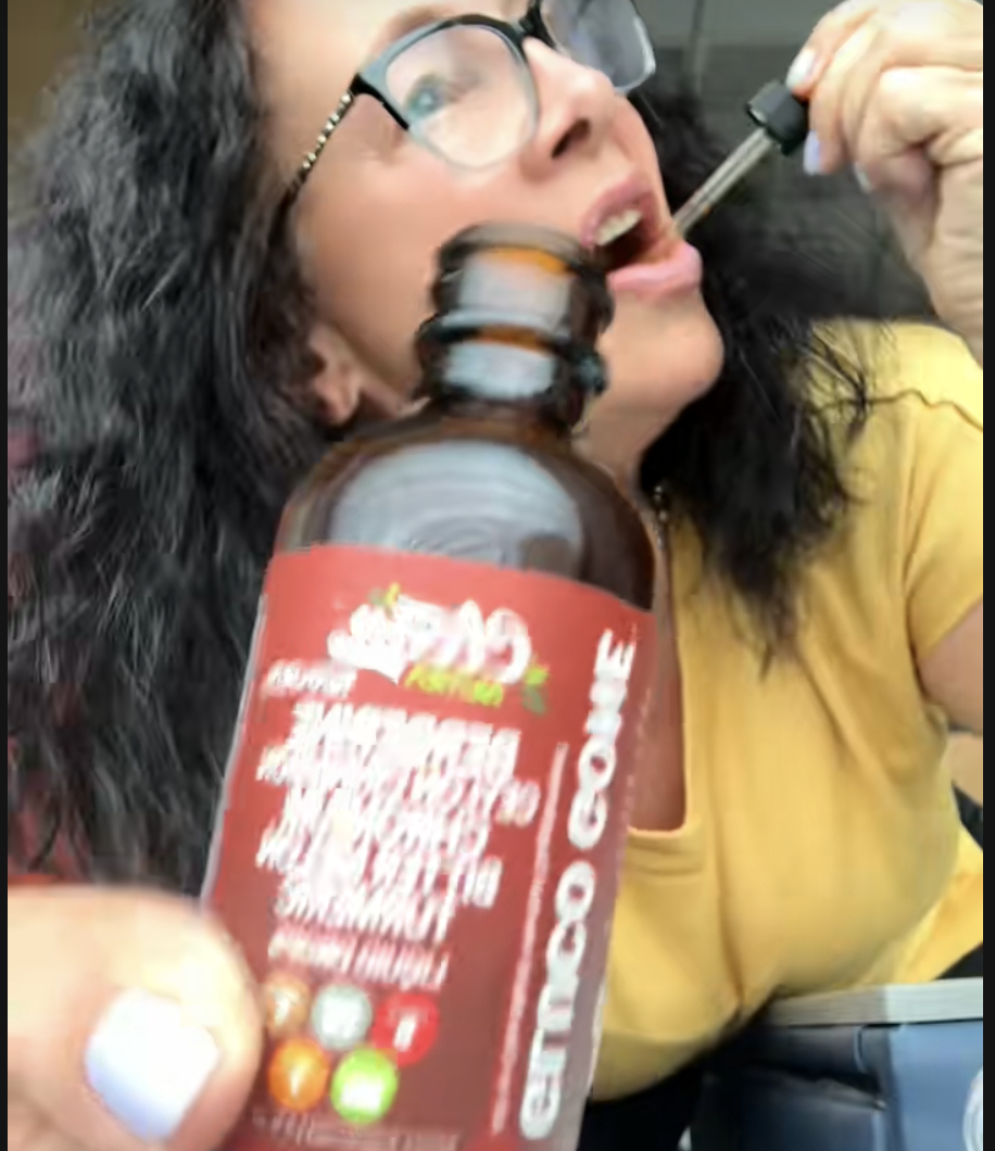 Woman using a dropper bottle labeled 'GMO GONE.'