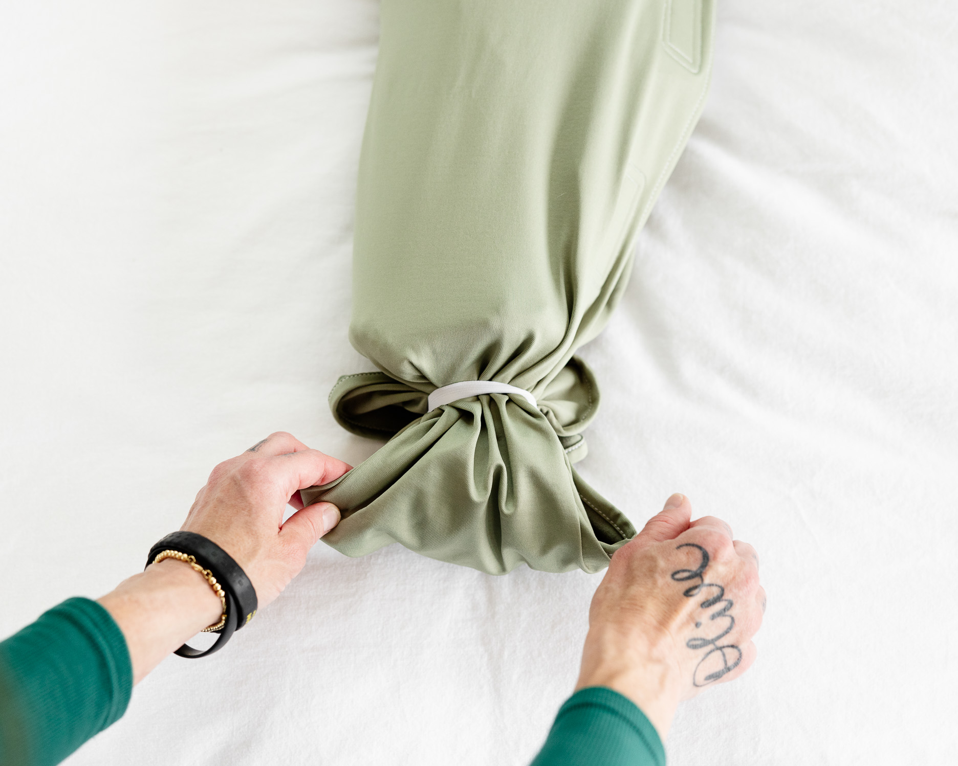 Overhead view of hands with tattoos tying a bundle of light green fabric with an elastic band.