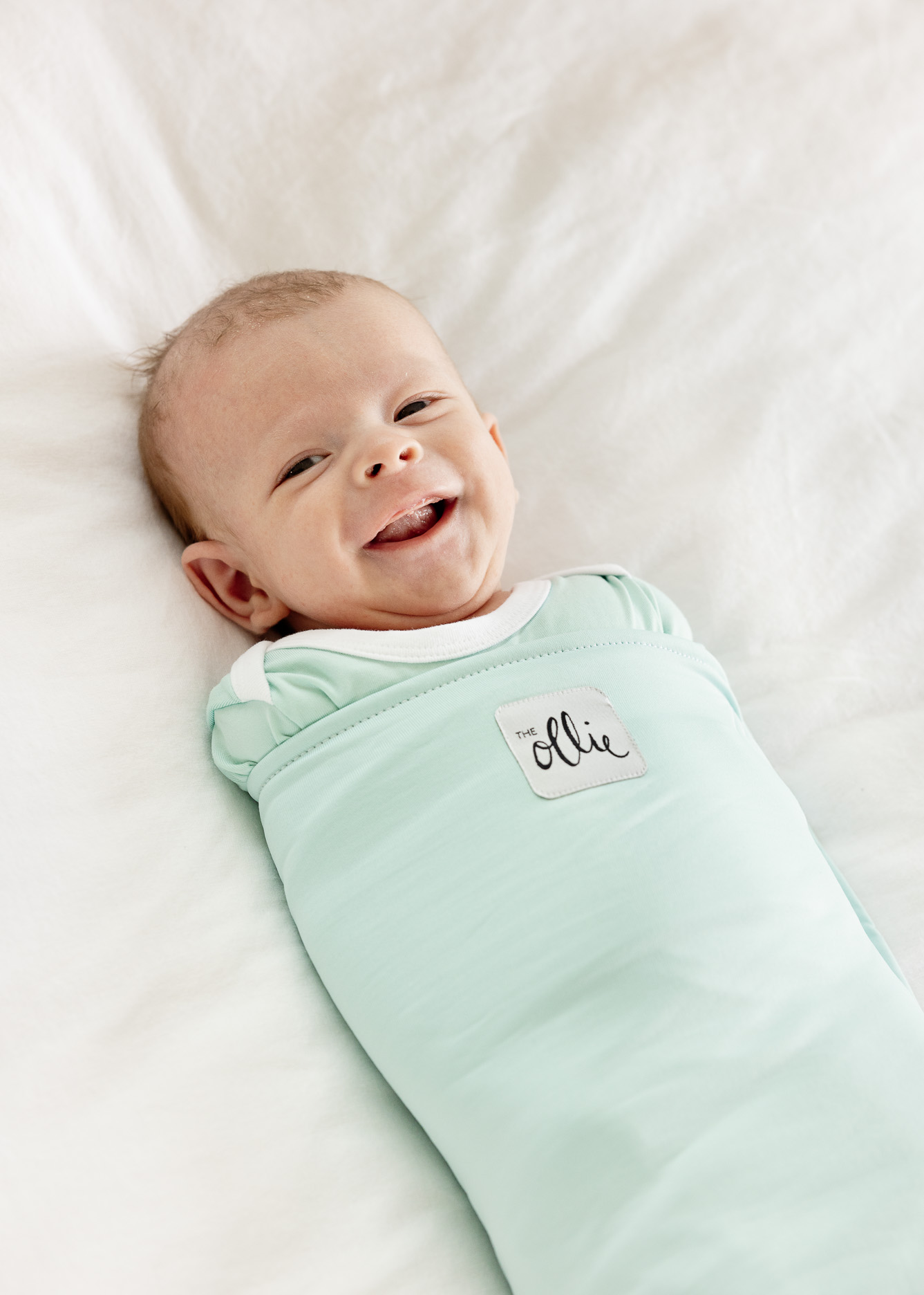 Smiling baby wrapped in a light green blanket.