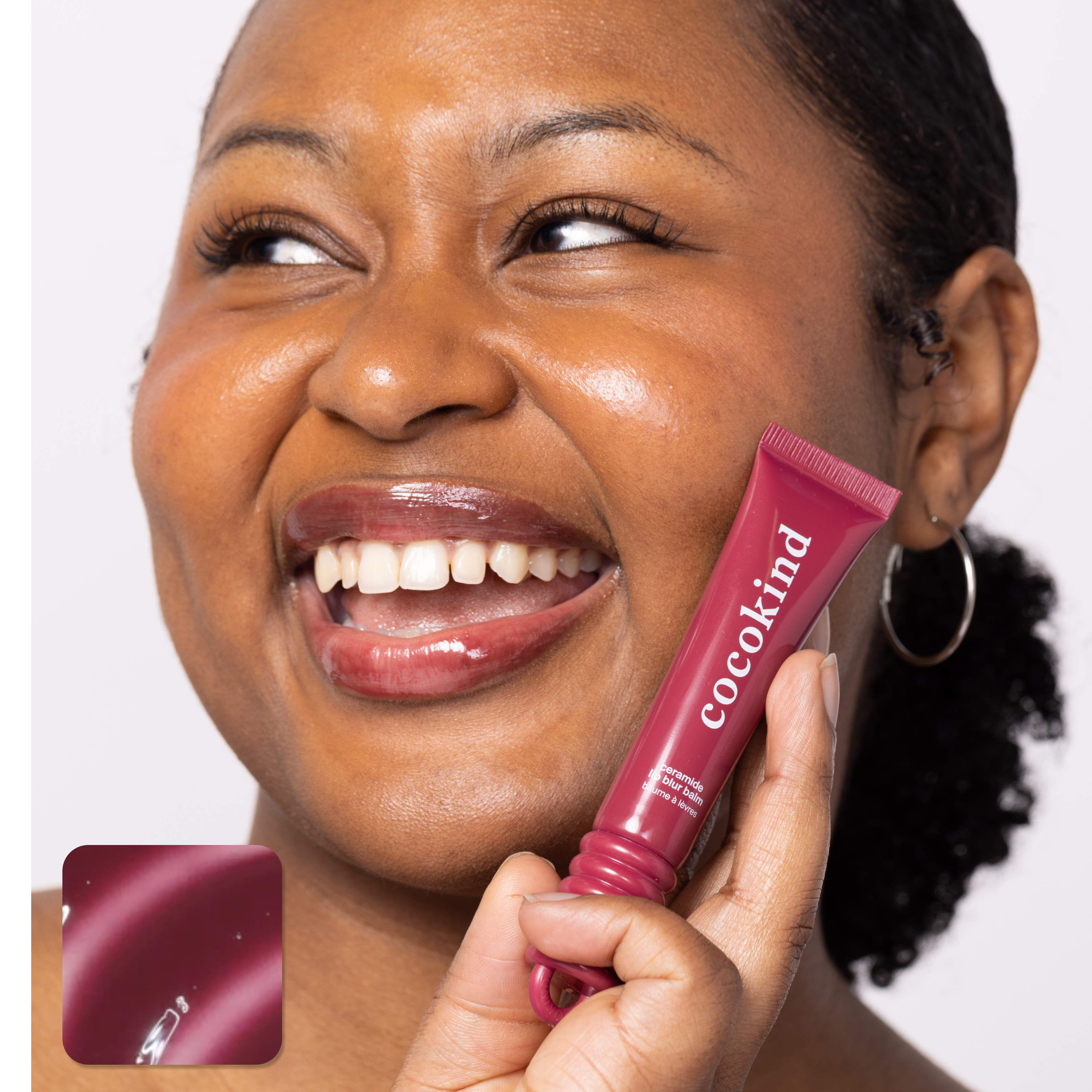 A person smiling and holding a red Cocokind lip balm tube.