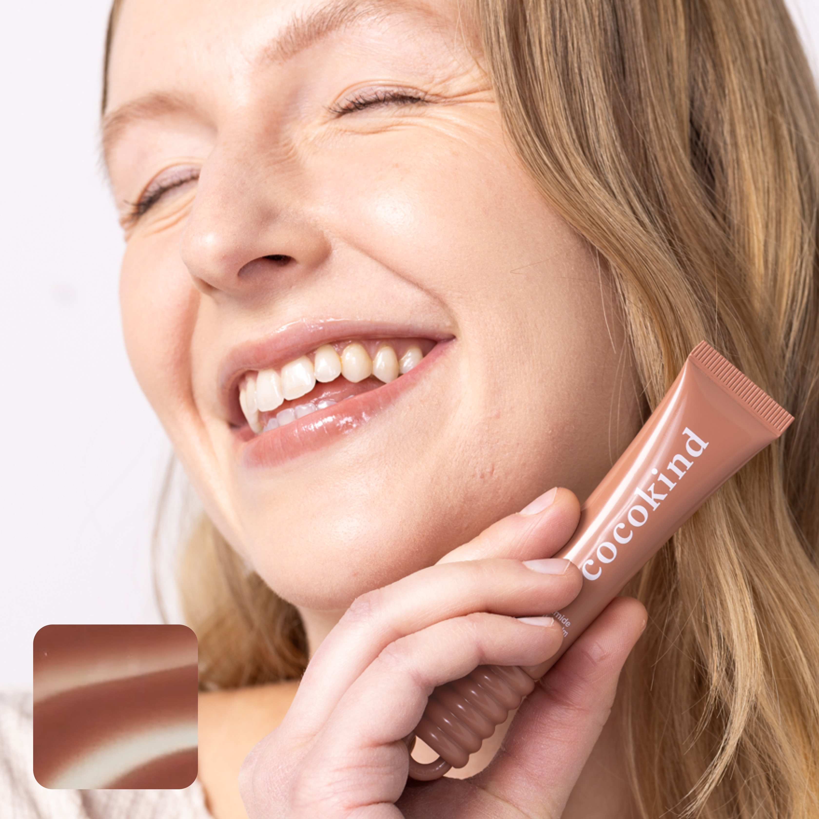 Person smiling while holding a Cocokind skincare tube.