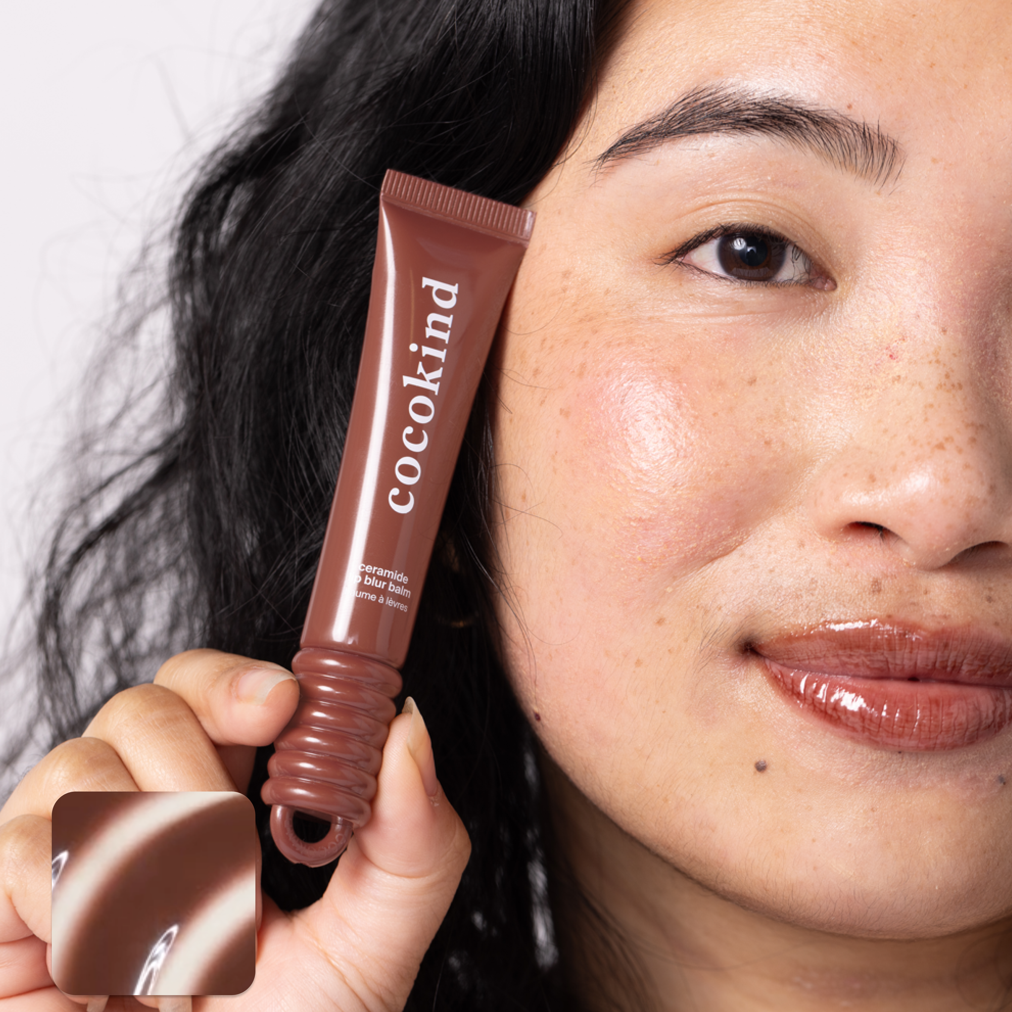 A person holding a tube of Cocokind ceramide blur balm near their face.