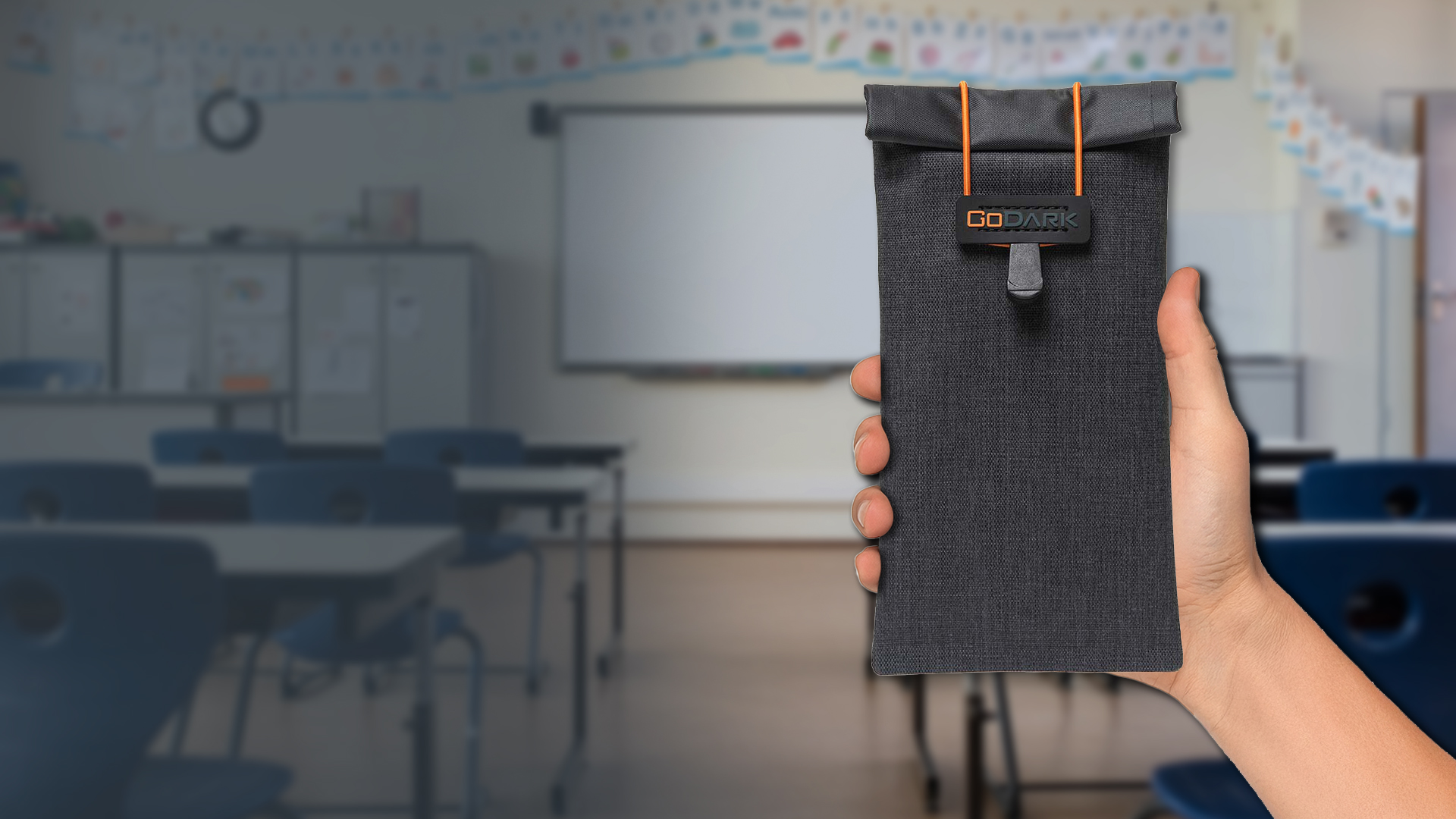 Hand holding GoDark Faraday Phone Bag, classroom in background
