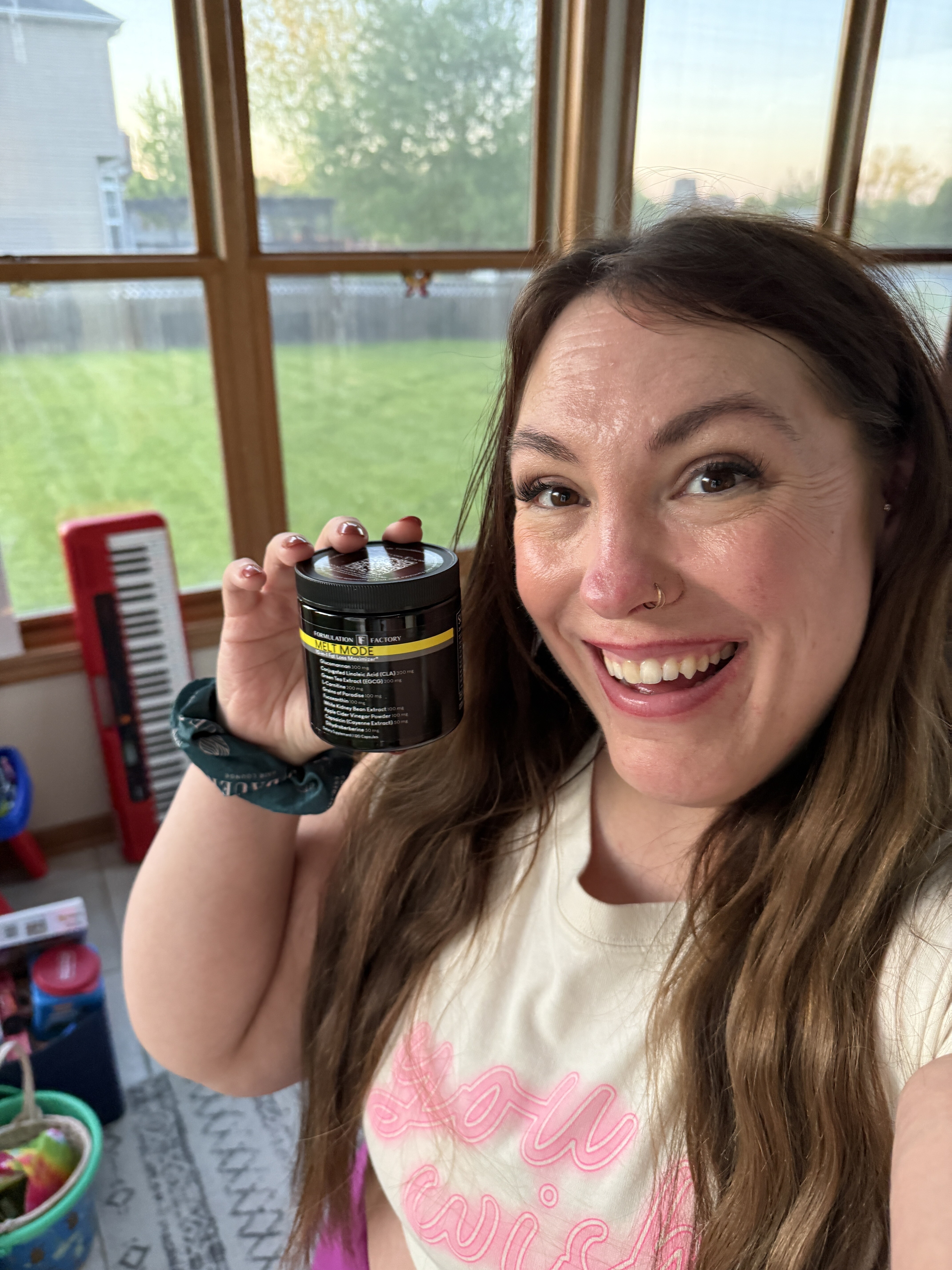 Smiling person holding a jar indoors with a window view of a lawn.
